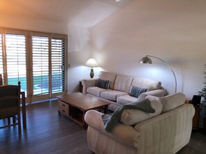 A living room with a sofa, a coffee table, and a lamp. There is a chair and a plant in the corner. - Great location on 11th Fairway! (Palm Desert)
