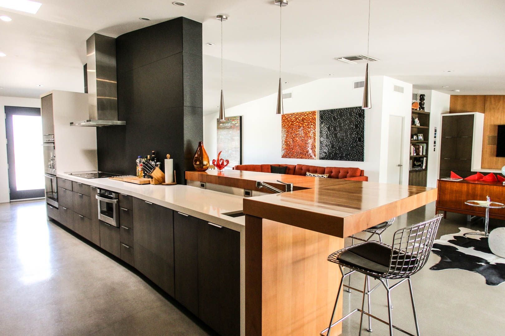 Une cuisine moderne dotée d’un îlot central, de meubles de couleur sombre, d’appareils électroménagers en acier inoxydable et d’un coin repas avec des tabourets de bar.