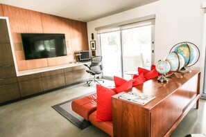 A modern living room with a flat-screen TV, a wooden cabinet, a leather sofa, and a desk with a globe. - Beautiful and Spacious El Paseo Pool Home (Palm Desert)
