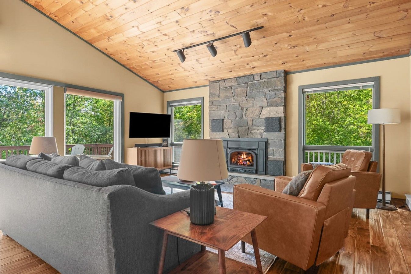 A modern living room with a stone fireplace, large windows, and a cozy seating area.
