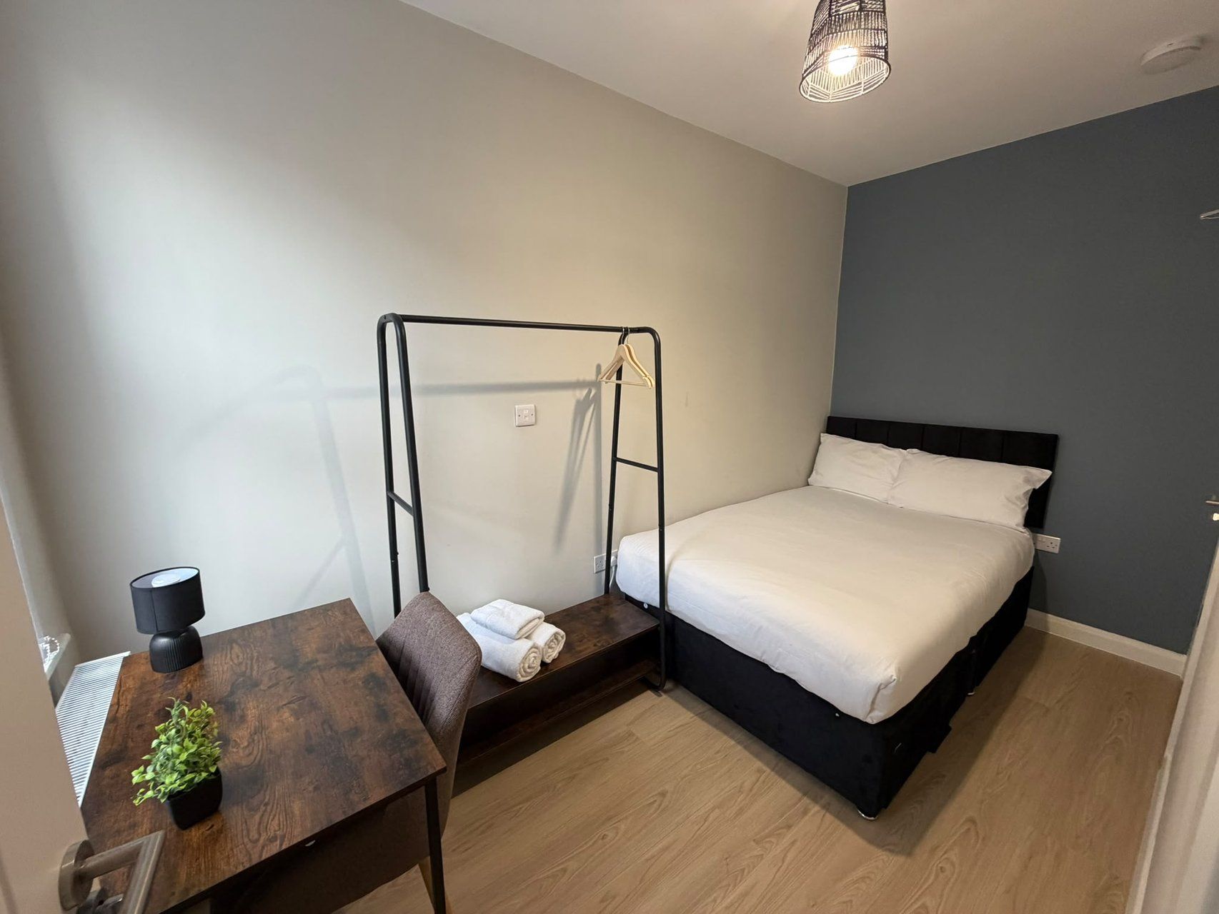 Ein Schlafzimmer mit einem Bett, einem Schreibtisch mit Stuhl, einer Pendelleuchte und einer kleinen Pflanze.
