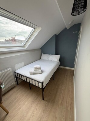 Una habitación pequeña con cama individual, techo inclinado, ventana y radiador.