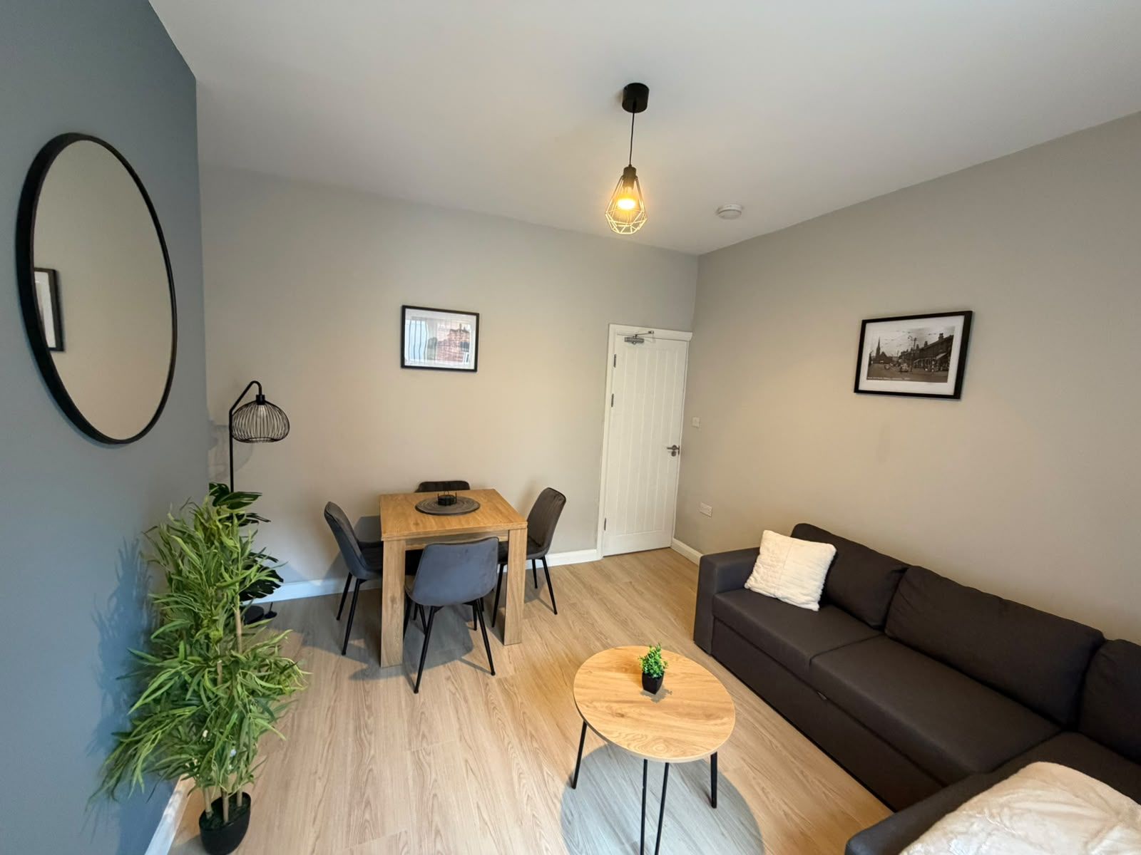 Una sala moderna con un sofá, una mesa de comedor con sillas, una pequeña mesa redonda con una planta, una maceta y dos cuadros en la pared.
