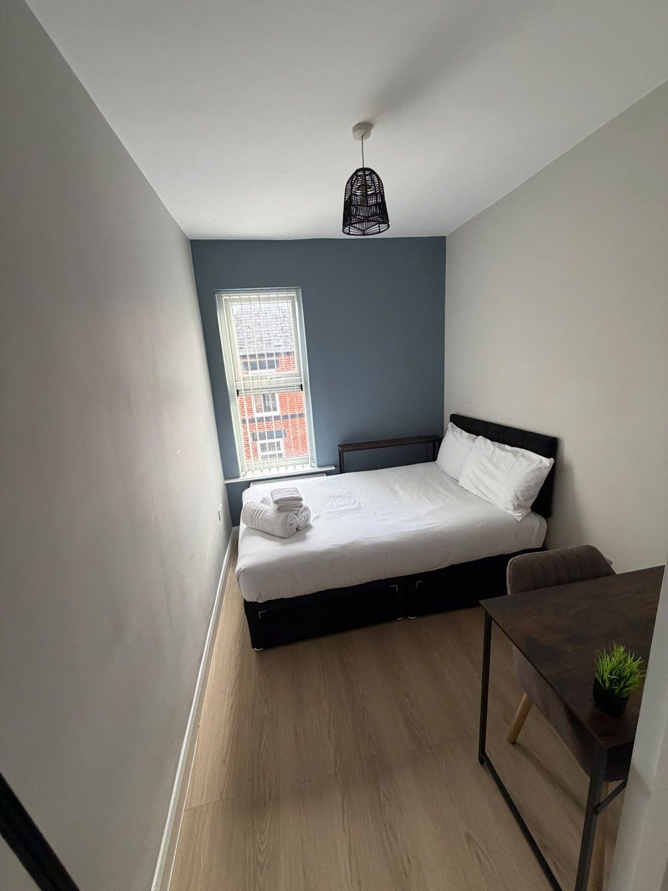 A small, modern bedroom with a single bed, a small table, and a window with a view of a building.