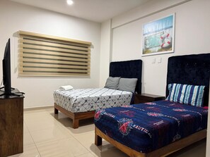 A hotel room with two beds, a television on a wooden stand, a window with blinds, and a painting on the wall. - 2-BEDROOM APARTMENT IN MAZATLÁN / SWIMMING POOL AND ROOFTOP WITH OCEAN VIEWS (Mazatlán)