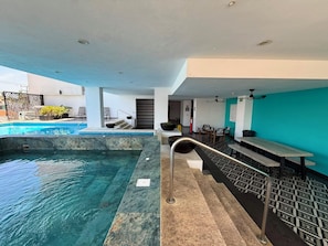 A swimming pool with a marble border, a seating area with tables and chairs, and a staircase leading to an upper level. - 2-BEDROOM APARTMENT IN MAZATLÁN / SWIMMING POOL AND ROOFTOP WITH OCEAN VIEWS (Mazatlán)