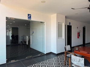 A hotel lobby with a glass door entrance, a fire extinguisher, a ceiling fan, and a patterned rug. - 2-BEDROOM APARTMENT IN MAZATLÁN / SWIMMING POOL AND ROOFTOP WITH OCEAN VIEWS (Mazatlán)