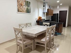 A dining area with a wooden table and chairs, a kitchen in the background, and a framed artwork on the wall. - 2-BEDROOM APARTMENT IN MAZATLÁN / SWIMMING POOL AND ROOFTOP WITH OCEAN VIEWS (Mazatlán)