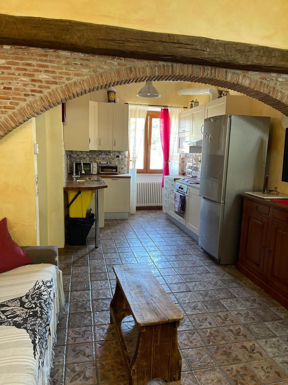 A kitchen with a wooden bench, a refrigerator, and a window with curtains.