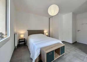 A bedroom with a bed, bedside lamps, a heater, and a hanging light fixture. - 300m from ski slopes, 1st floor, terrace, tv, ski locker, 58m², Serre Chevalier (Briançon)