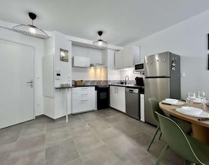 A modern kitchen with white cabinetry, a built-in oven, a refrigerator, and a dining area with a table set for two. - 300m from ski slopes, 1st floor, terrace, tv, ski locker, 58m², Serre Chevalier (Briançon)