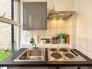 A kitchen with a stainless steel sink, a stove with four burners, and a window with a view of greenery. - Compact Split-Level Studio near Paddington (Greater London)