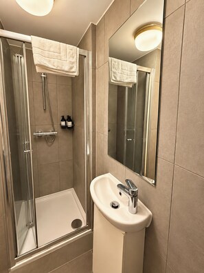 A modern bathroom with a glass shower enclosure, a sink with a mirror, and a towel rack. - Compact Split-Level Studio near Paddington (Greater London)