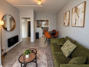 A living room with a sofa, a coffee table with a plant, a TV, and a dining area with chairs and a table. - Cosy One-Bedroom Flat near Paddington (Greater London)