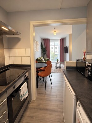 A modern kitchen with a built-in oven, a dining area with a table and chairs, and a view of the city through a window. - Cosy One-Bedroom Flat near Paddington (Greater London)