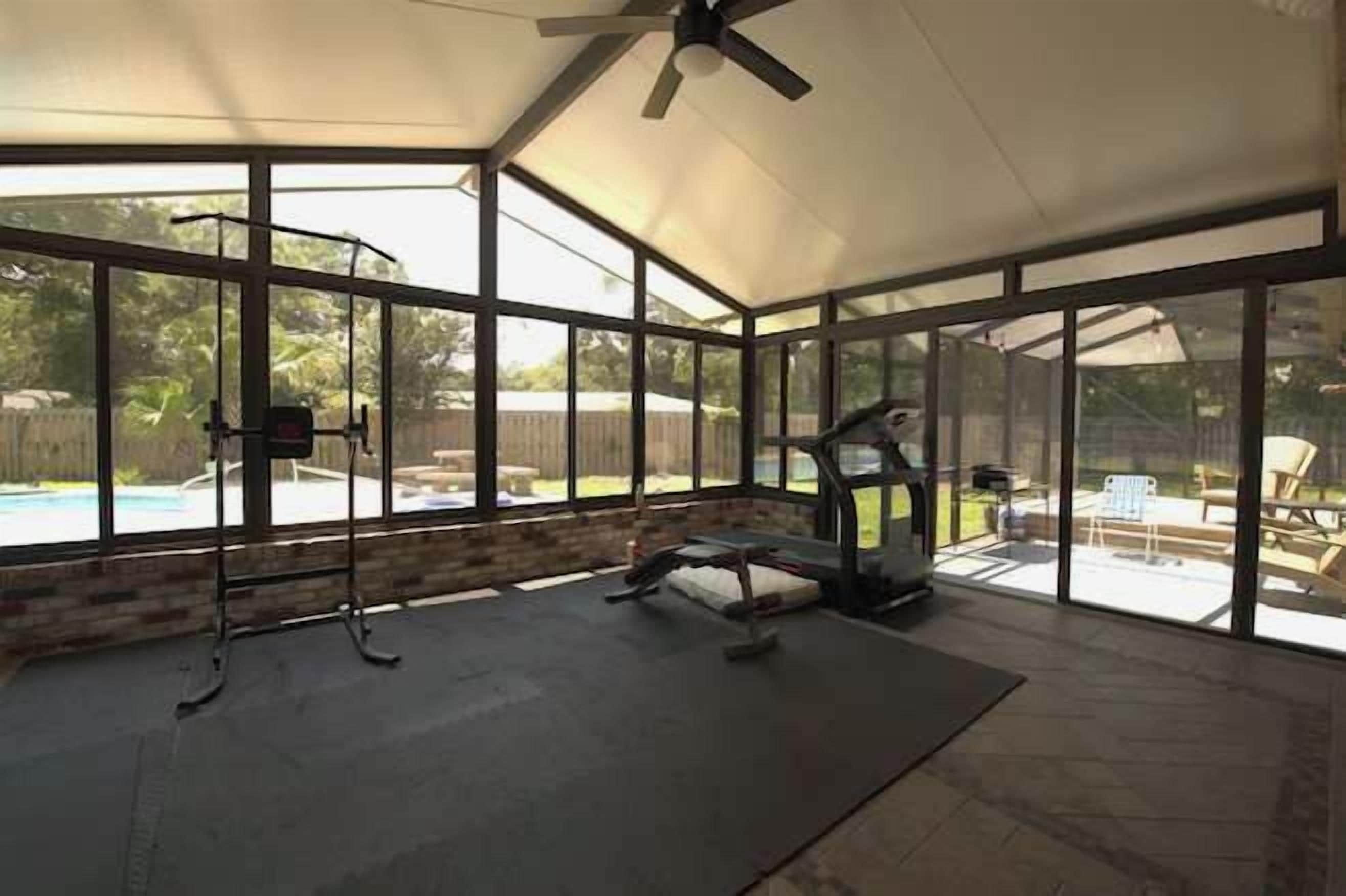 A covered patio with a view of a swimming pool, exercise equipment, and a ceiling fan.