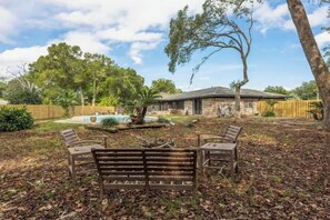 A backyard with a wooden bench, a small fountain, and a house with a stone exterior. - Pet Friendly Home with Private Pool, Home Gym, Ping Pong Table & Wifi (Fort Walton Beach)