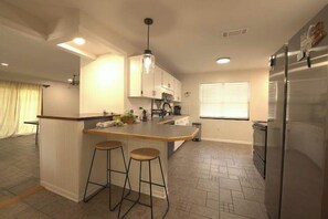 A kitchen with a central island, bar stools, a refrigerator, and a window with blinds. - Pet Friendly Home with Private Pool, Home Gym, Ping Pong Table & Wifi (Fort Walton Beach)