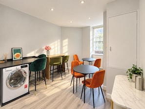 A modern kitchen with a washing machine, a dining area with chairs, and a window providing natural light. - Boutique Room in the Heart of Soho (Greater London)