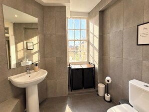 A modern bathroom with a sink, mirror, toilet, and a window providing natural light. - Cool Soho Room Steps from Chinatown & West End (Greater London)