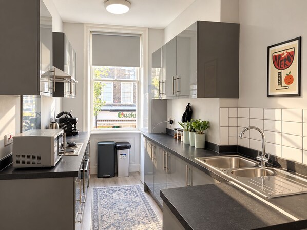 A modern kitchen with a built-in microwave, a sink, and a window overlooking a sushi restaurant. - Boutique-Style Room in London’s West End IV (Greater London)