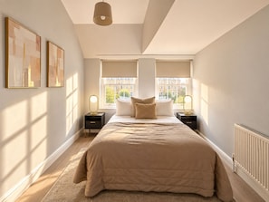 A bedroom with a large bed, two bedside tables with lamps, a window with blinds, and artwork on the wall. - Boutique-Style Room in London’s West End IV (Greater London)
