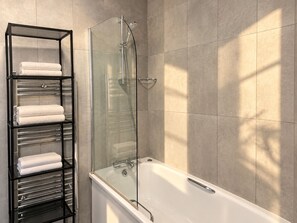 A modern bathroom with a glass-enclosed shower, a white bathtub, and a metal towel rack with folded towels. - Boutique-Style Room in London’s West End IV (Greater London)