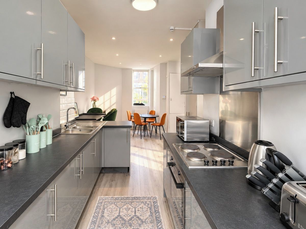 A modern kitchen with stainless steel appliances, a central island, and a dining area with orange chairs.