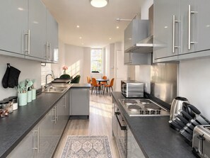 Una cocina moderna con electrodomésticos de acero inoxidable, una isla central y un comedor con sillas anaranjadas.