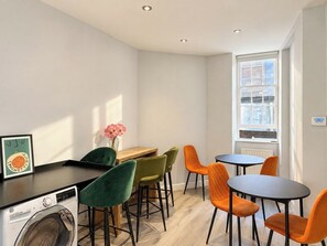 A compact room with a washing machine, a small table, and chairs. - Soho Hideaway | Private Room near West End (Greater London)