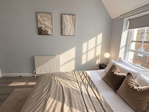 A bedroom with a bed, pillows, a radiator, and two wall-mounted artworks. - Soho Hideaway | Private Room near West End (Greater London)