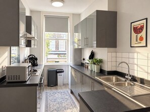 A modern kitchen with stainless steel appliances, a double sink, and a view to the outside. - Soho Hideaway | Private Room near West End (Greater London)