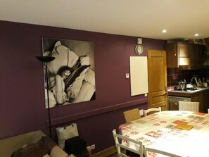 A room with a dining table, chairs, a bed, a large abstract painting, a clock, and a kitchen area. - 180m from ski slopes, Ground floor, balcony, fireplace or stove, parking, ski locker, 65m², Valloire (Valloire)