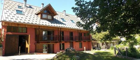 A two-story building with a red facade, a balcony, and a gravel driveway.