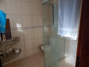 Un baño con cabina de ducha de vidrio, inodoro y lavamanos, con una toalla colgada en la pared.