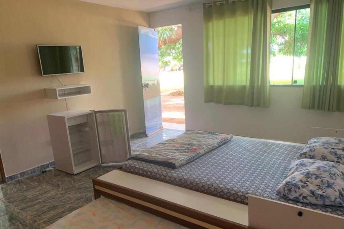 A bedroom with a bed, a TV mounted on the wall, a wardrobe, and a window with curtains.