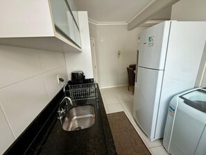 A compact kitchen with a stainless steel sink, a white refrigerator, and a microwave. - Comfortable apartment on Palmas beach. (Governador Celso Ramos)