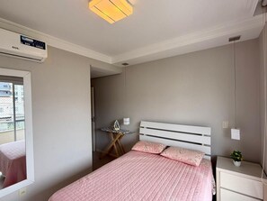 Ein Schlafzimmer mit einem Bett, einem Nachttisch, einem kleinen Tisch mit einem Bügeleisen und einem Fenster.