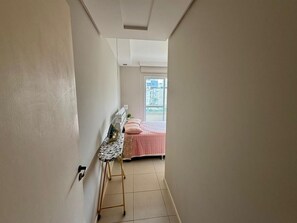 A narrow hallway leading to a bedroom with a bed and a small table with a picture frame. - Comfortable apartment on Palmas beach. (Governador Celso Ramos)