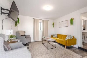 Ein Wohnzimmer mit Sofa, Sessel, Couchtisch und einem an der Wand befestigten Fernseher.