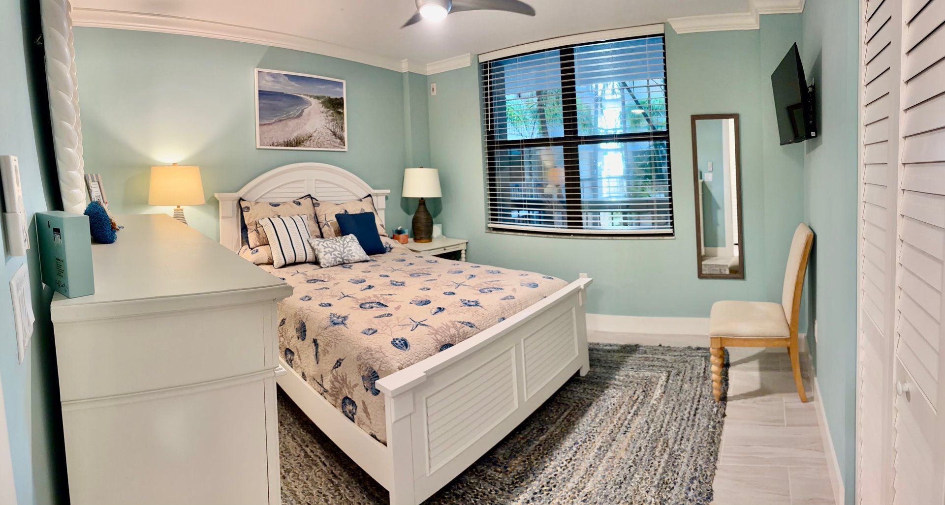 Een slaapkamer met een bed, nachtkastjes, een stoel, een raam met zonwering en een schilderij aan de muur.