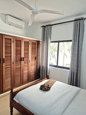 A bedroom with a bed, a ceiling fan, an air conditioning unit, and a window with curtains. - Beautiful 3-bedroom Beach Front apartment with AC in vibrant Mombasa County (Mombasa County)