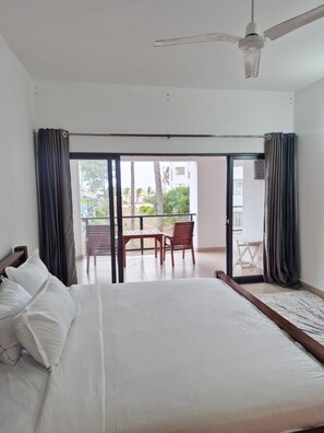 A hotel room with a bed, a ceiling fan, and a view of the outdoor area through a sliding glass door. - Beautiful 3-bedroom Beach Front apartment with AC in vibrant Mombasa County (Mombasa County)