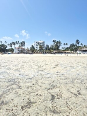 A beach with clear skies, palm trees, and buildings in the background. - Beautiful 3-bedroom Beach Front apartment with AC in vibrant Mombasa County (Mombasa County)