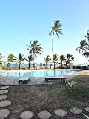 A pool area with lounge chairs and palm trees. - Beautiful 3-bedroom Beach Front apartment with AC in vibrant Mombasa County (Mombasa County)