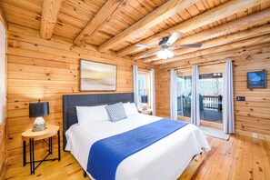 Een houten slaapkamer met een bed, een plafondventilator en uitzicht door de glazen deur.