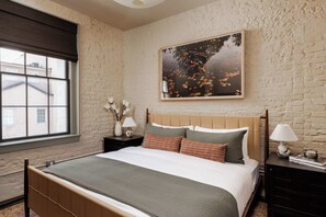 A bedroom with a large bed, a nightstand with a lamp, a vase with flowers, and a painting on the wall. - Newly Renovated CBD Condo, Near French Quarter (New Orleans)