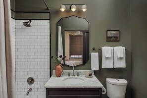 A bathroom with a shower, a sink with a vase of flowers, a mirror, and towels. - Newly Renovated CBD Condo, Near French Quarter (New Orleans)