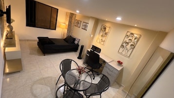 A compact living space with a bed, a dining table with chairs, a desk, and decorative wall art.