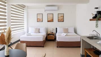 Habitación de hotel con dos camas, una mesita, una silla, un escritorio con lavamanos y obras de arte en la pared.